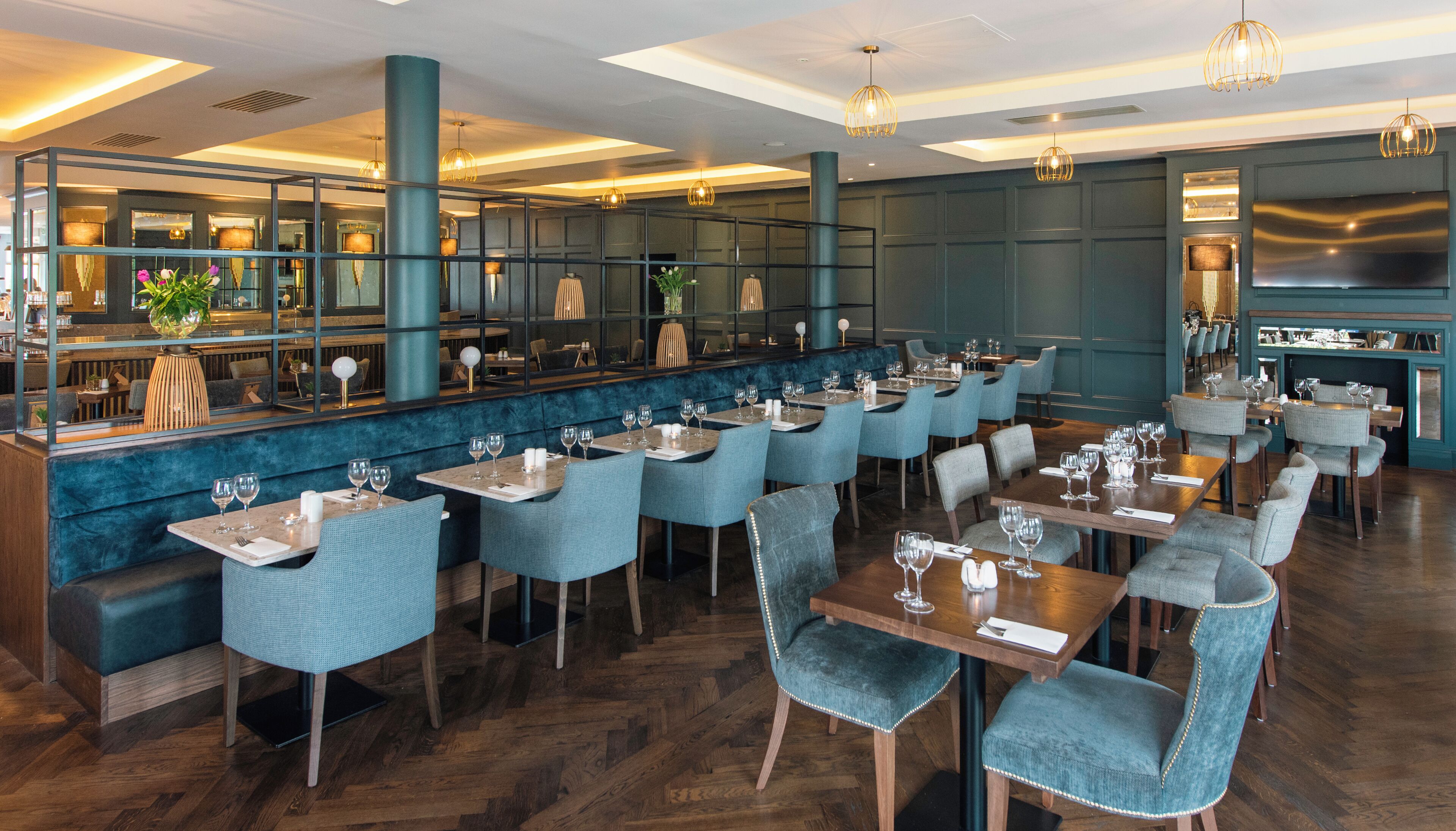 A restaurant with multiple tables and chairs, a bar area, and a large television screen.