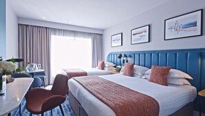 Une chambre d’hôtel avec deux lits, un bureau et une chaise. Deux tableaux encadrés sont accrochés au mur.