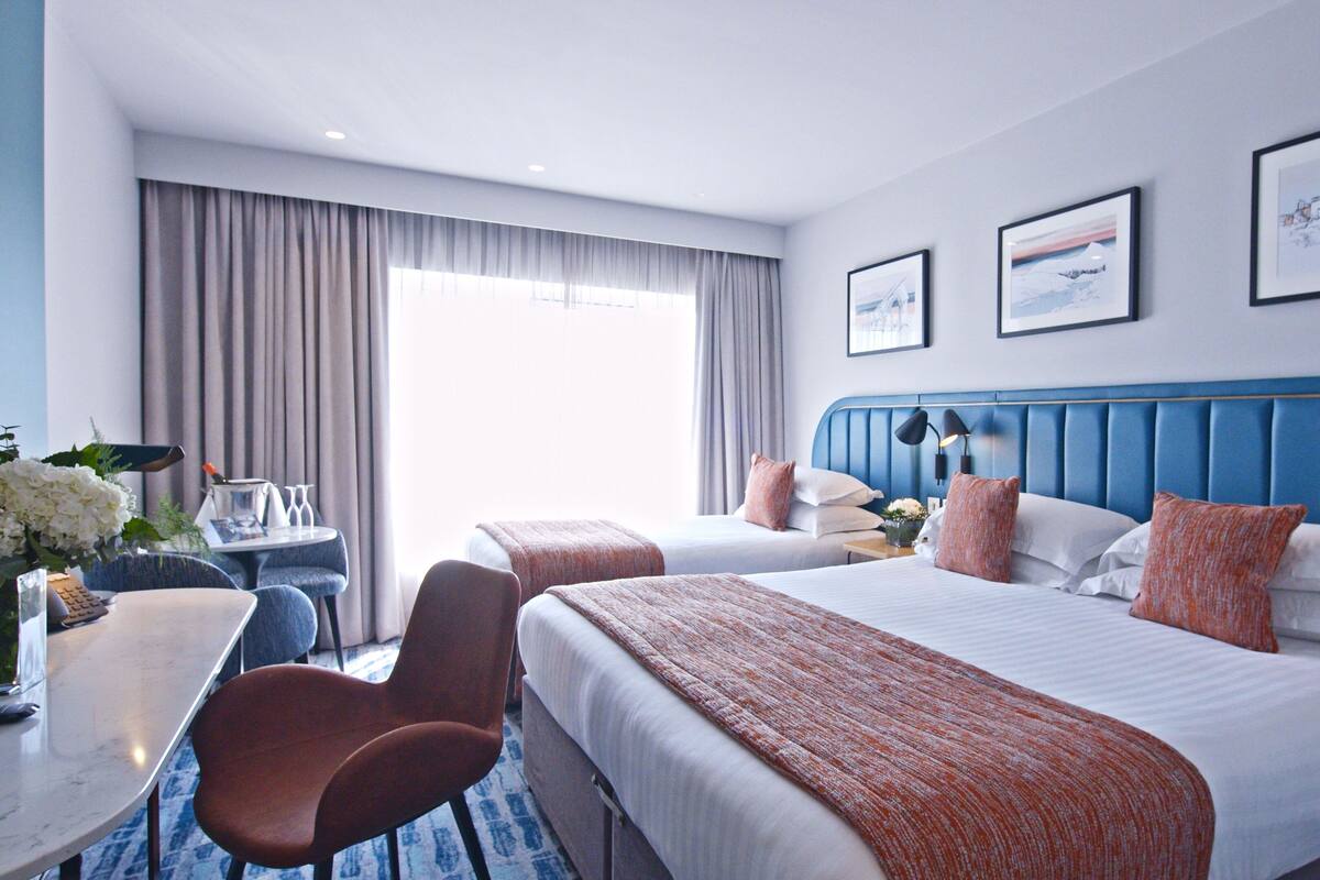 Une chambre d’hôtel avec deux lits, un bureau et une chaise. Deux tableaux encadrés sont accrochés au mur.