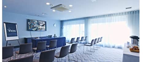 A conference room with a blue carpet, a projector screen, a table with chairs, and a large window with curtains.