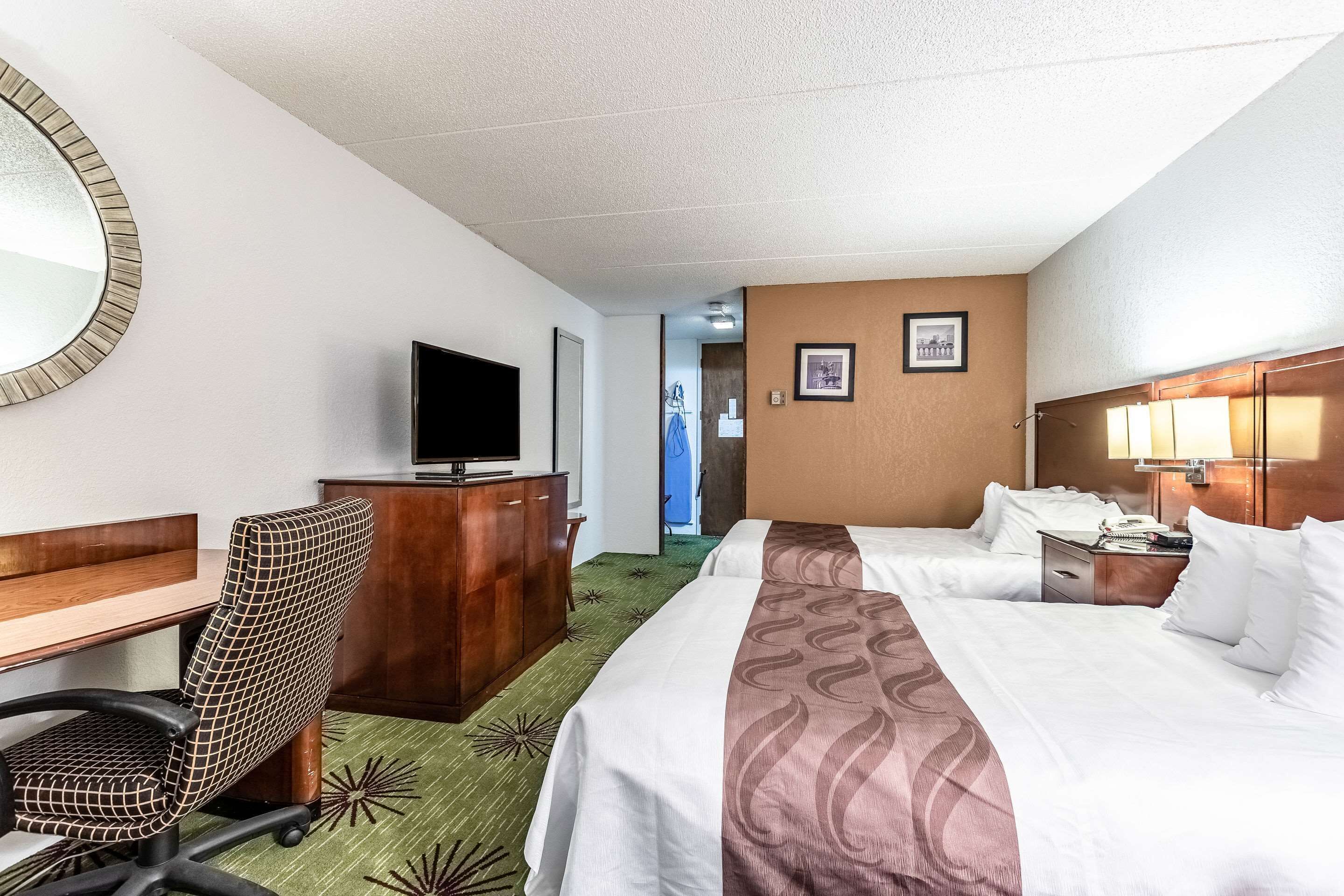 A hotel room with two beds, a desk, a chair, a television, and a mirror.