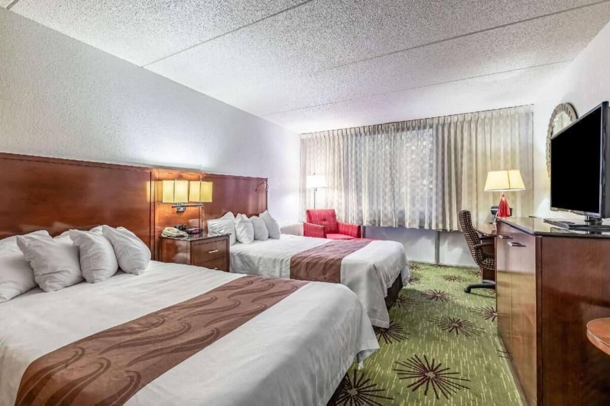 A hotel room with two beds, a desk, a TV, a chair, and a window with curtains.