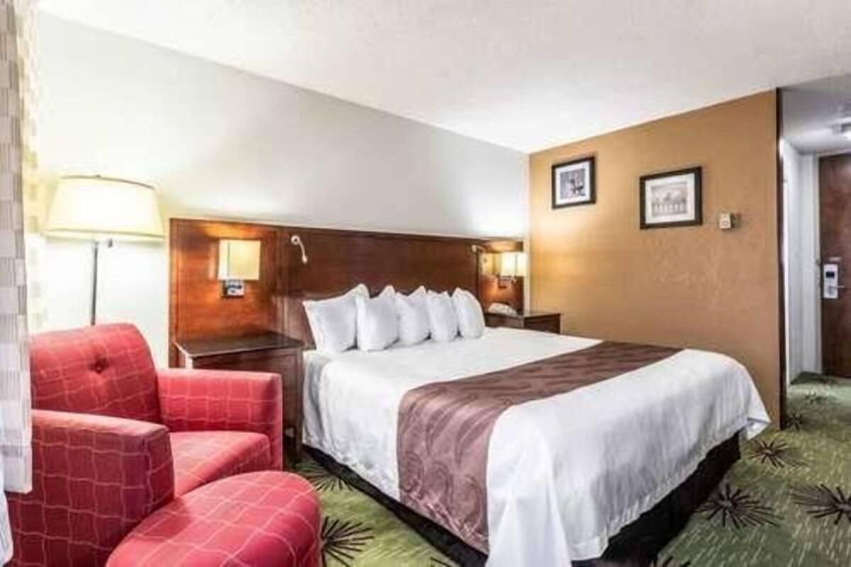 A hotel room with a bed, a red armchair, a nightstand, and a lamp.
