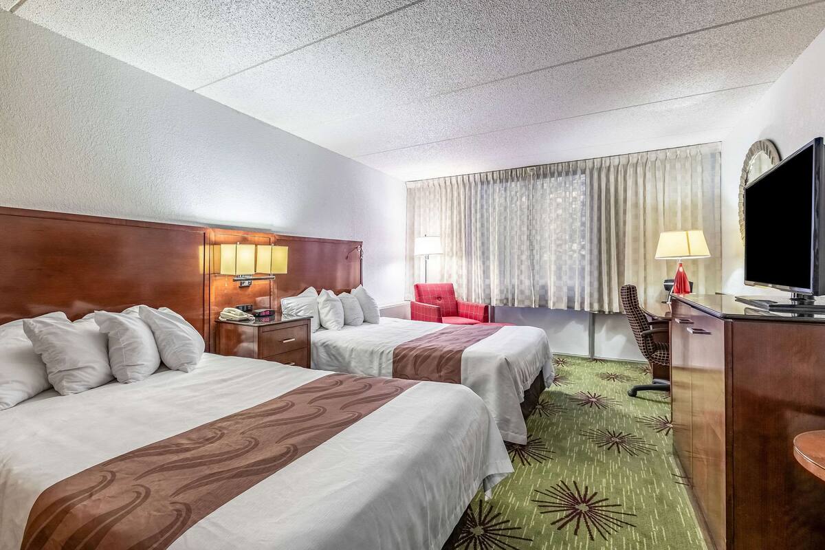 A hotel room with two beds, a desk, a chair, a television, and a window with curtains.