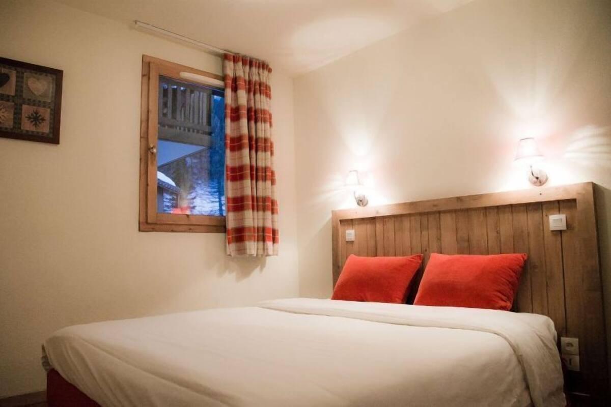 Un dormitorio con cama, ventana con vistas y un aplique de pared.