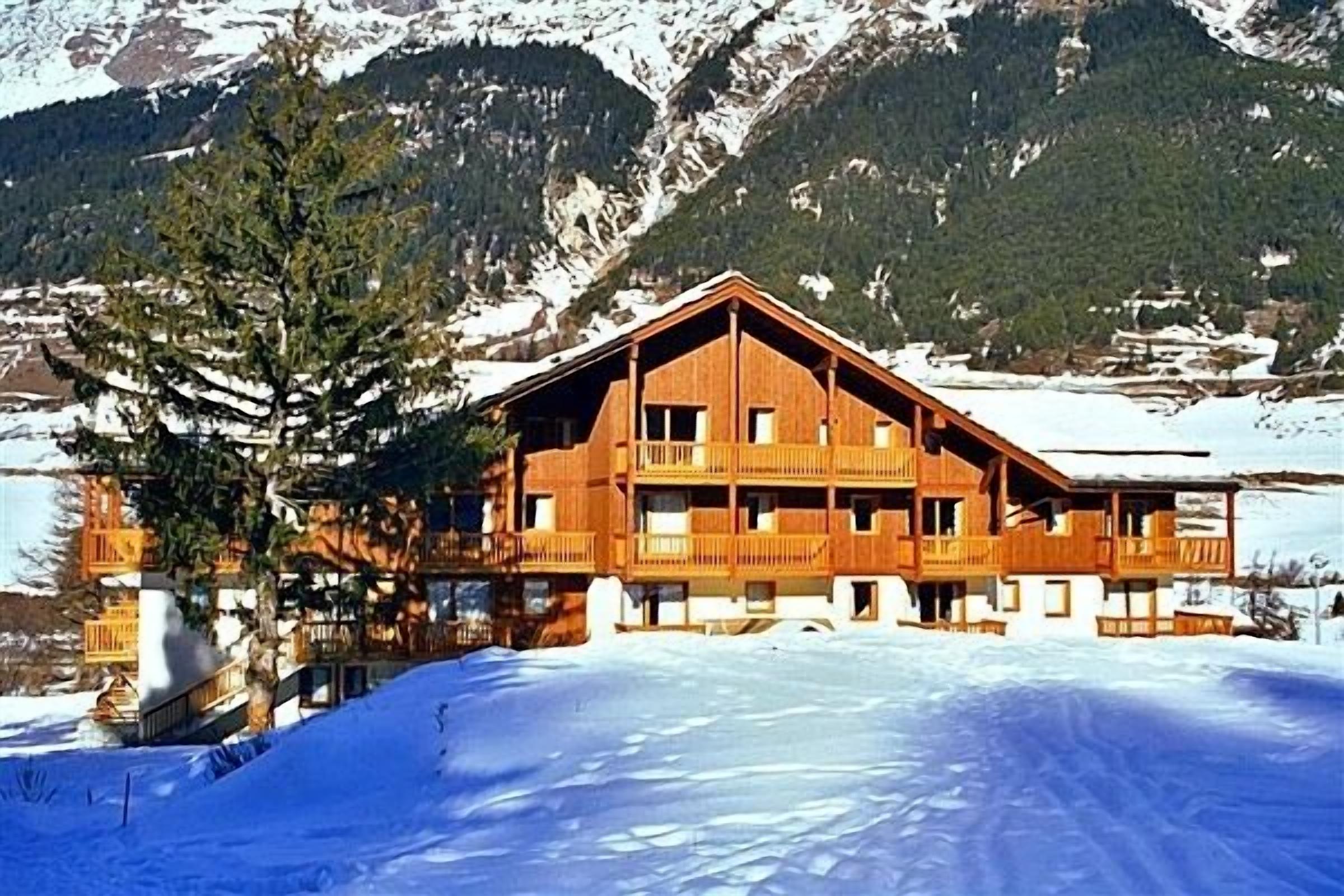 Un chalet en bois doté de plusieurs balcons, situé au pied d’une montagne enneigée.