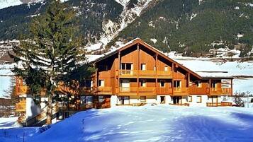 Un chalet en bois doté de plusieurs balcons, situé au pied d’une montagne enneigée.