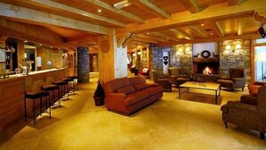 Um interior acolhedor com lareira de pedra, vigas de madeira, um espaço de bar e assentos confortáveis.