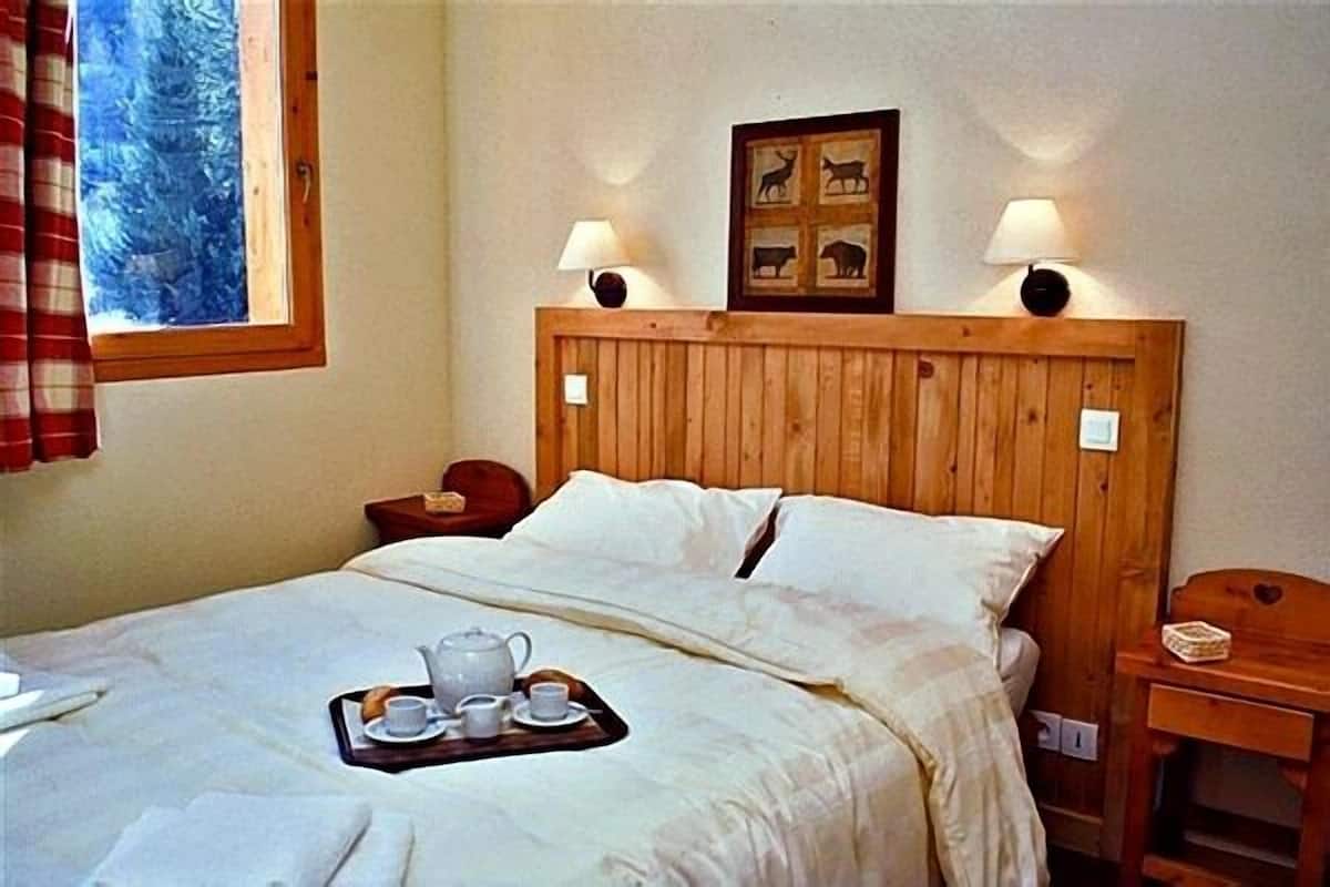 Una cama bien hecha con una bandeja de té y tazas, un cabecero de madera y un cuadro enmarcado sobre la cama.
