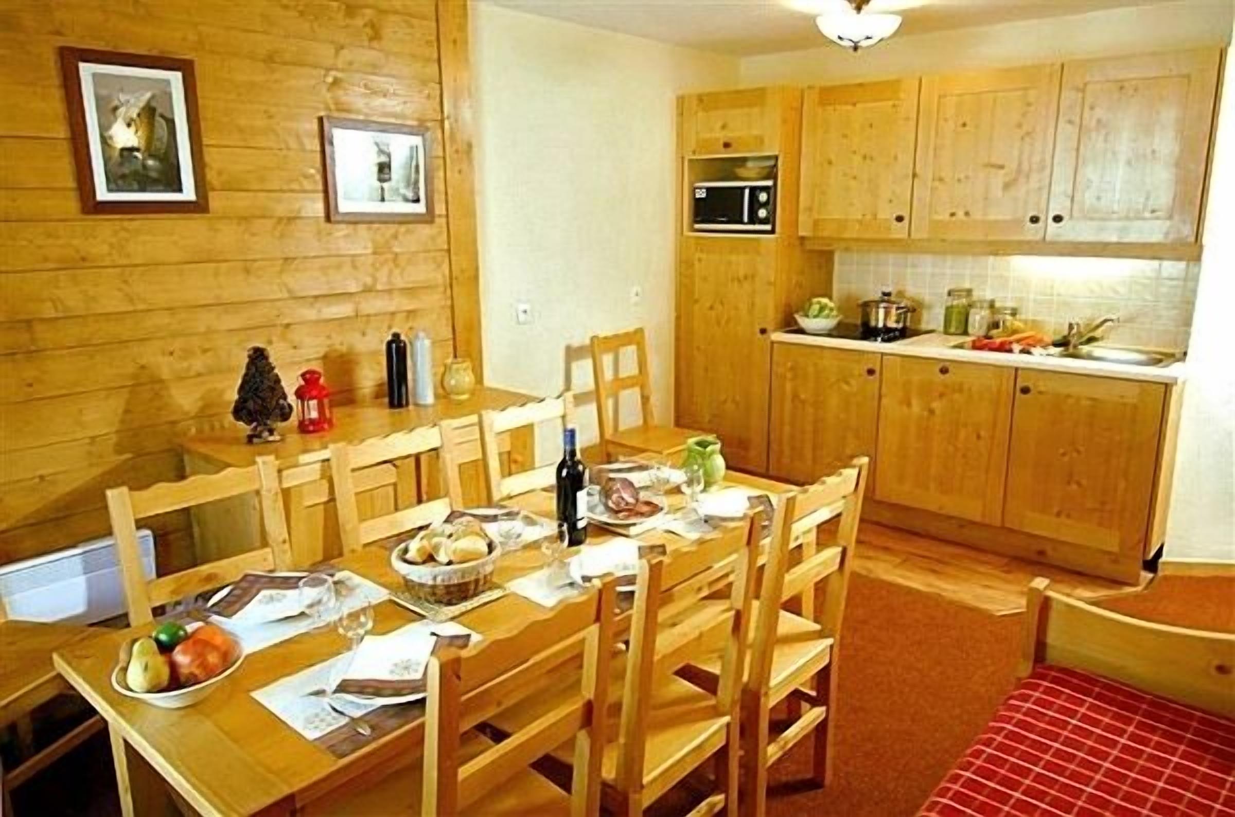 Una mesa de comedor de madera con sillas, una zona de cocina con armarios de madera y un microondas.