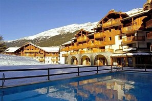Un hotel con varias terrazas de madera, piscina y una montaña nevada al fondo.
