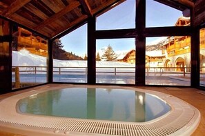 Un jacuzzi con vistas a un paisaje nevado de montaña a través de amplios ventanales.
