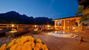 A wooden deck with lounge chairs, a hot tub, and a wooden cabin with glass doors. - Hotel Hochfilzer (Ellmau)