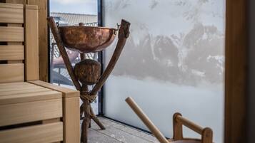 Un banco de madera y un cuenco de madera con una cuchara de madera sobre un suelo de piedra, con vista a la montaña a través de un ventanal grande.