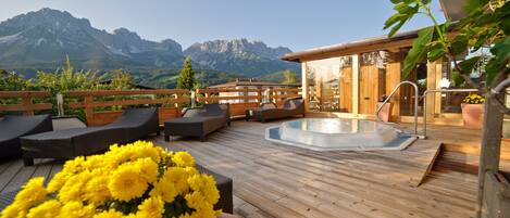 A wooden deck with lounge chairs, a hot tub, and a view of mountains.