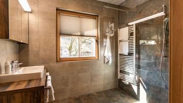 A modern bathroom with a large window, a shower with a glass door, and a wooden vanity.