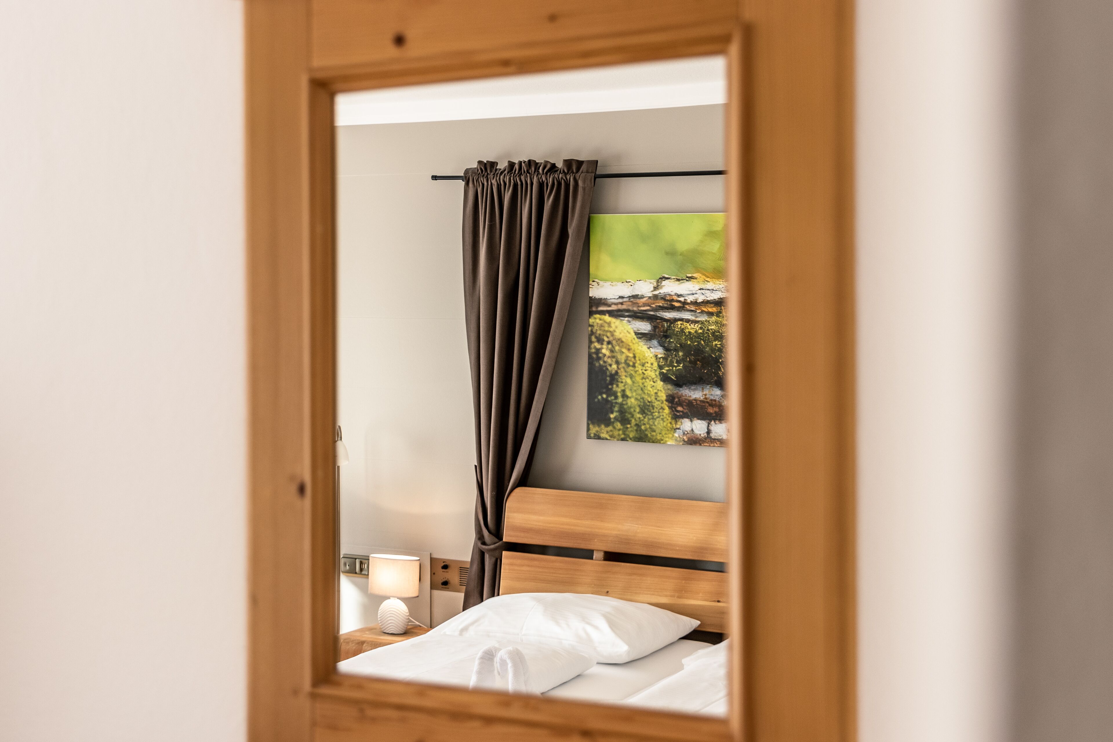 Un dormitorio con cabecera de madera, una cama con ropa de cama blanca, una mesita de noche con una lámpara y un cuadro de un paisaje en la pared.