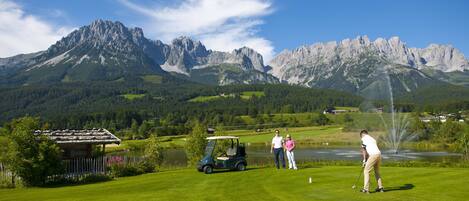 Un campo de golf con un lago, montañas y un pabellón.