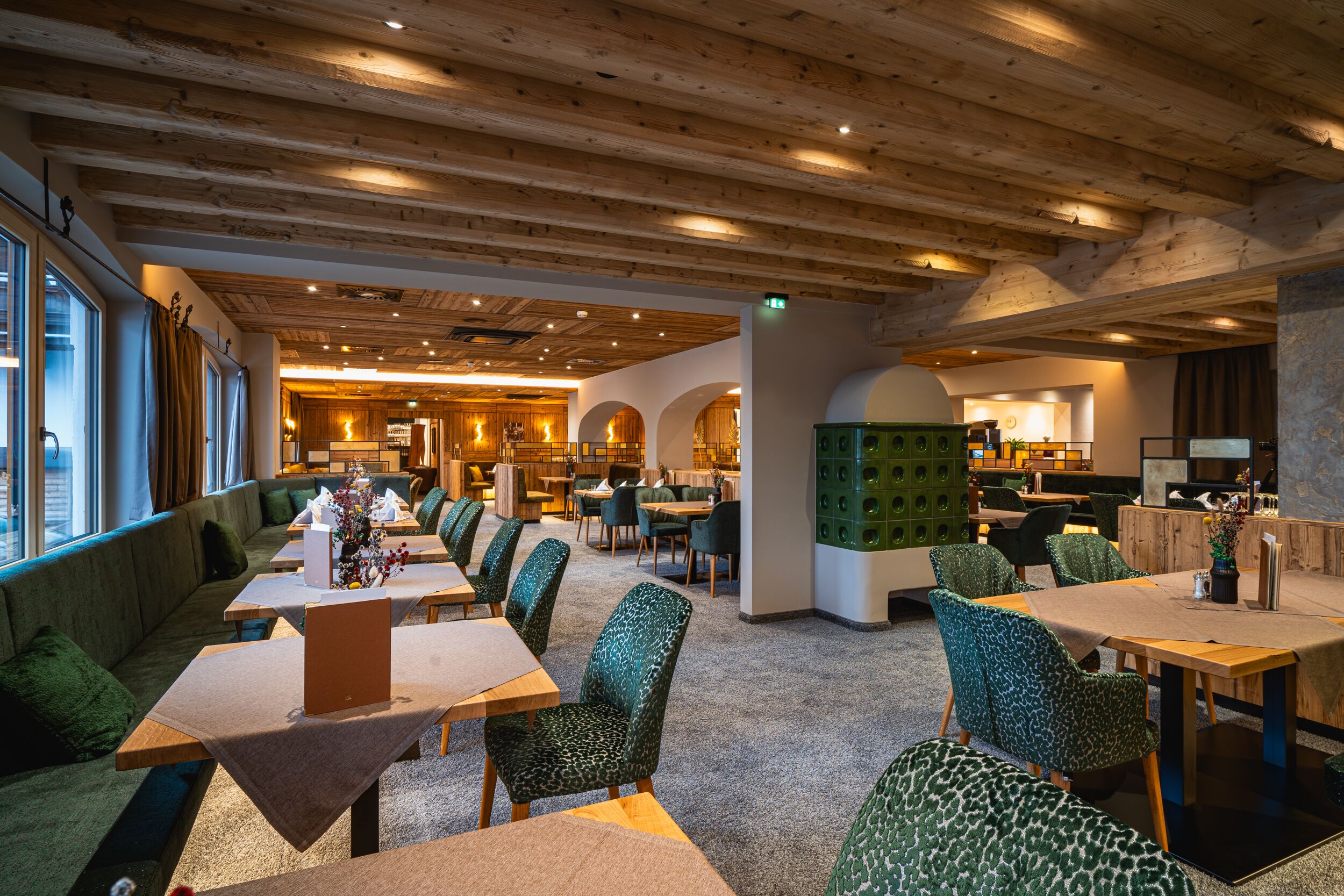 A spacious library with wooden beams, green upholstered chairs, and tables with a laptop on one.