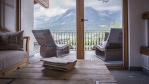 A balcony with wicker chairs and a wooden table, overlooking a mountainous landscape. - Hotel Hochfilzer (Ellmau)