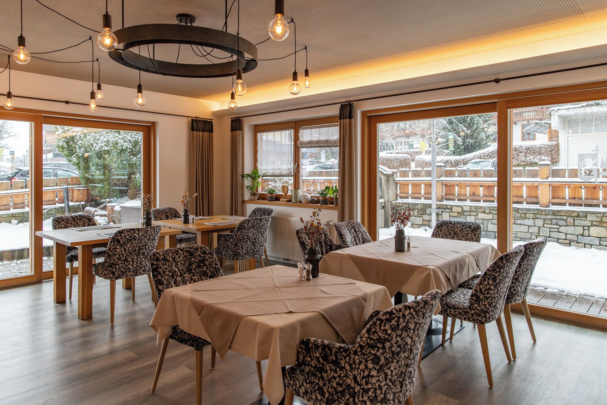 Een restaurant met twee tafels, gestreepte stoelen en grote ramen met uitzicht op een besneeuwde straat.