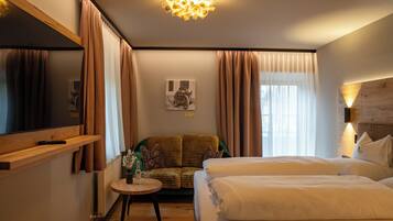 Ein Hotelzimmer mit Bett, Sofa, einem kleinen Tisch mit Vase, einem Bild an der Wand und einem Fernseher auf der linken Seite.
