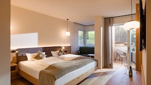 A modern bedroom with a large bed, bedside tables, a small table with a bottle, and a view of a balcony. - Hotel Sonnschein (Hopfgarten im Brixental)