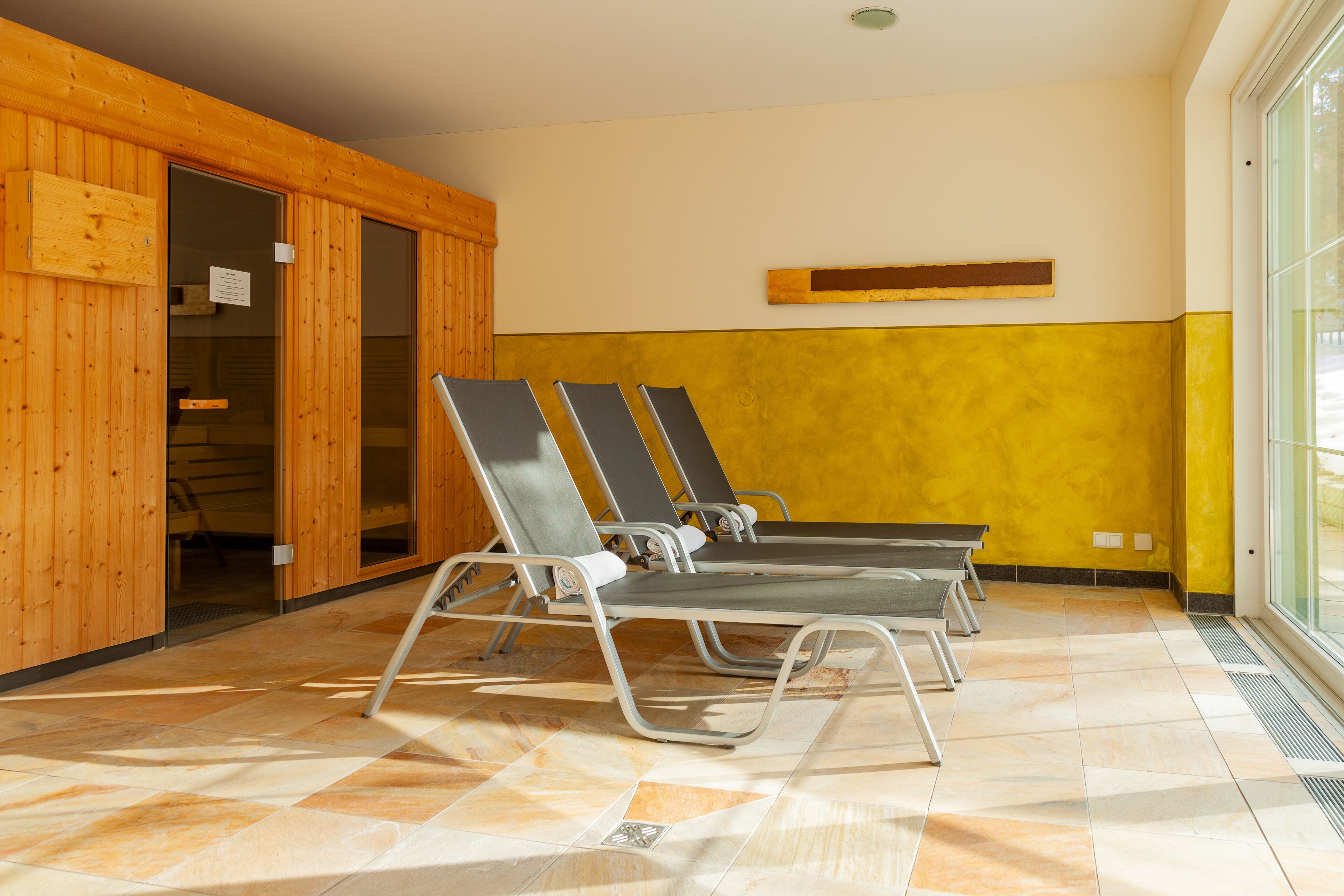 A room with wooden walls, a yellow accent wall, and a large window. There are three reclining chairs and a wooden door.
