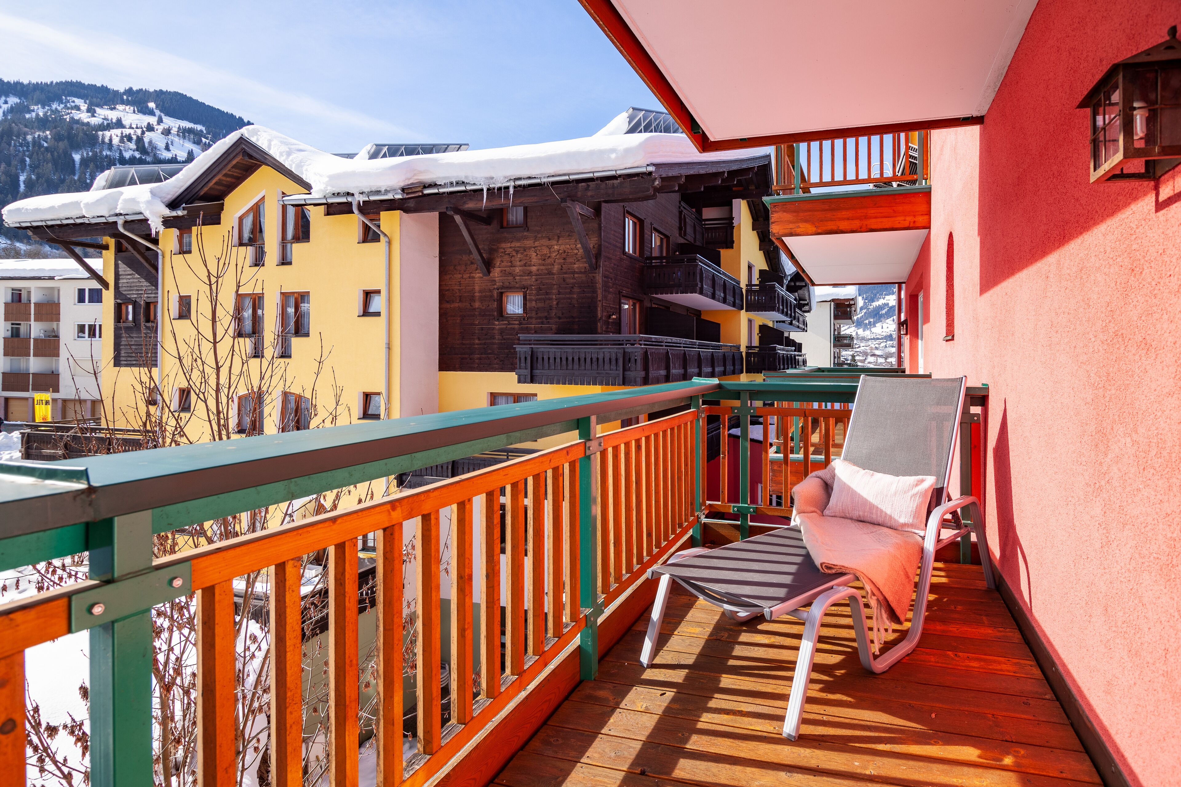 A wooden deck with a chair, a balcony with a railing, and a building with multiple windows and balconies.