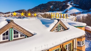 A hotel with a snow-covered roof and a view of a snowy mountain landscape. - Hotel Sonnschein (Hopfgarten im Brixental)