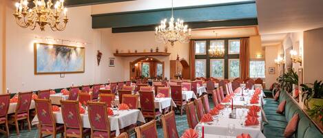 A formal dining room with multiple tables set for service, wooden chairs, and a green sofa.