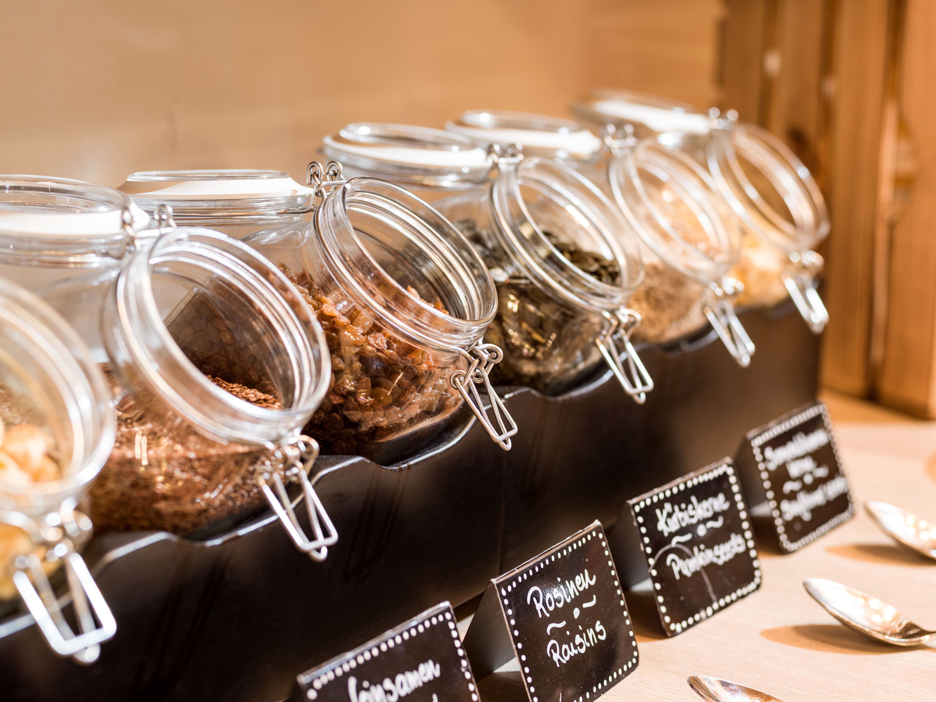 A row of glass jars with metal clasps, each labeled with different names of dried fruits.