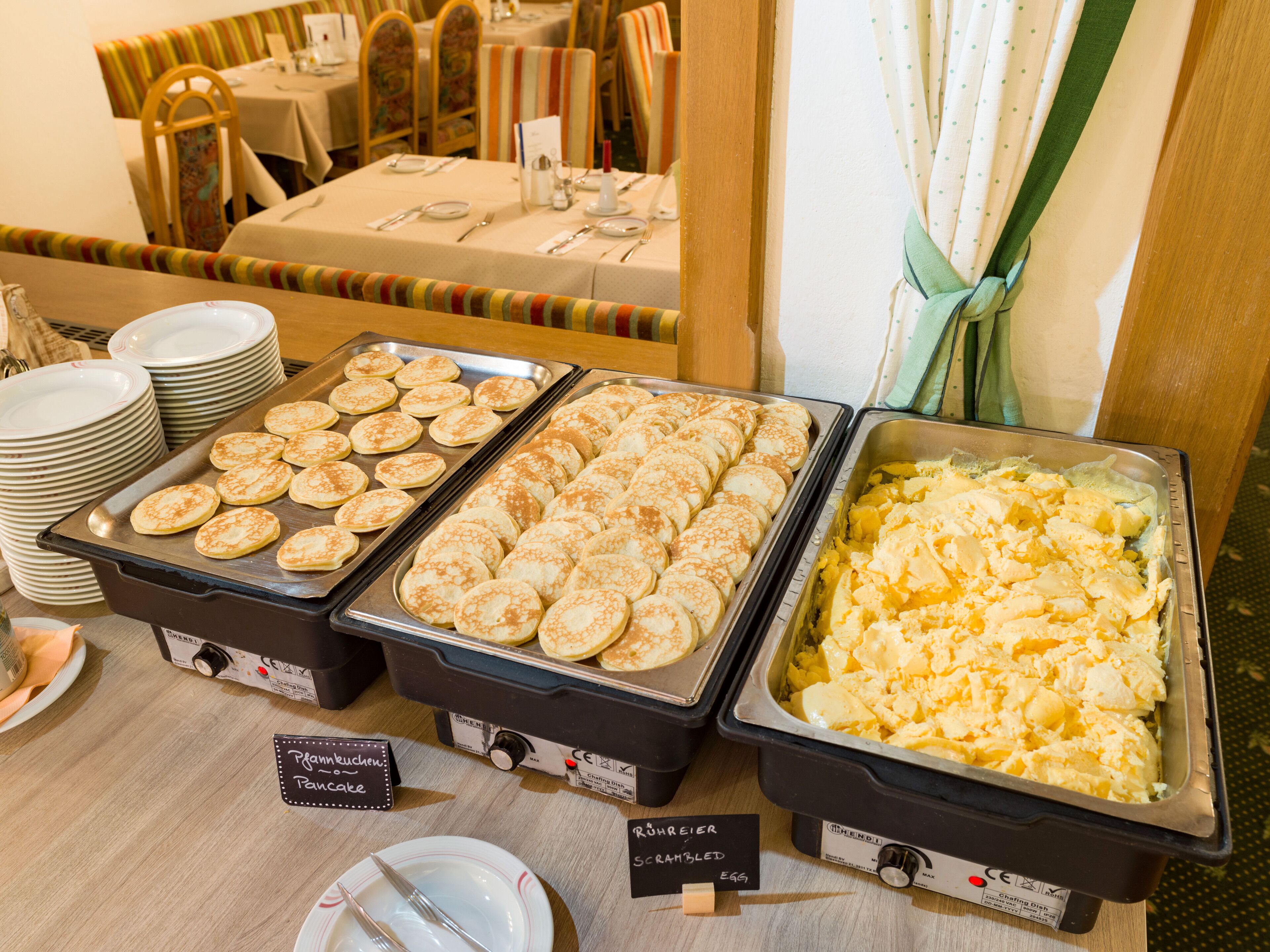 Un buffet con diverse pietanze, tra cui pancakes e uova strapazzate.