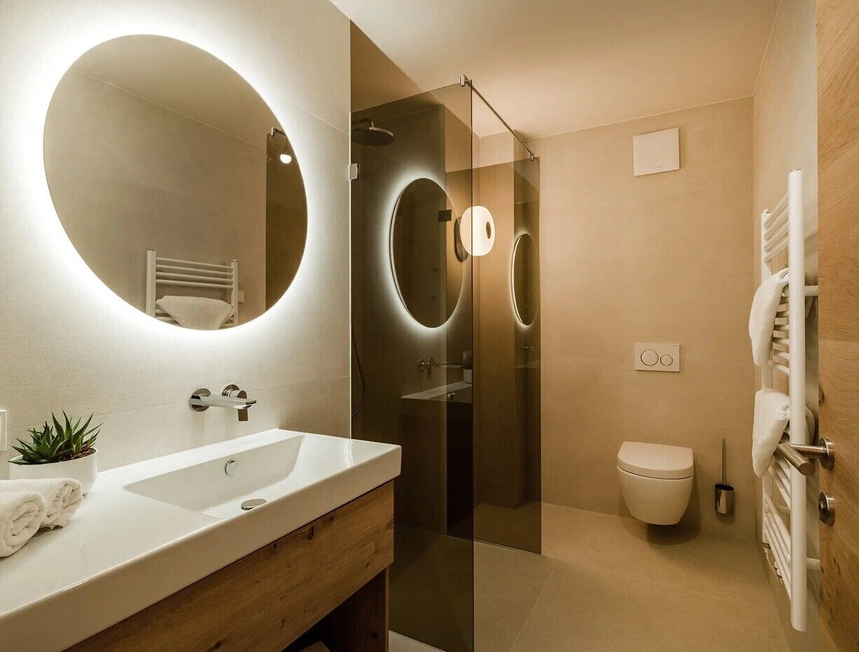 Un baño moderno con un espejo grande, un lavamanos, un inodoro y una ducha con mampara de cristal.