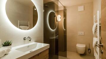 Un baño moderno con un espejo grande, un lavamanos, un inodoro y una ducha con mampara de cristal.