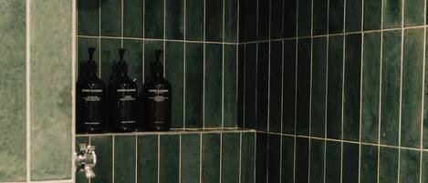 A bathroom with green tiles and three bottles of 'Grown Alchemist' shampoo.