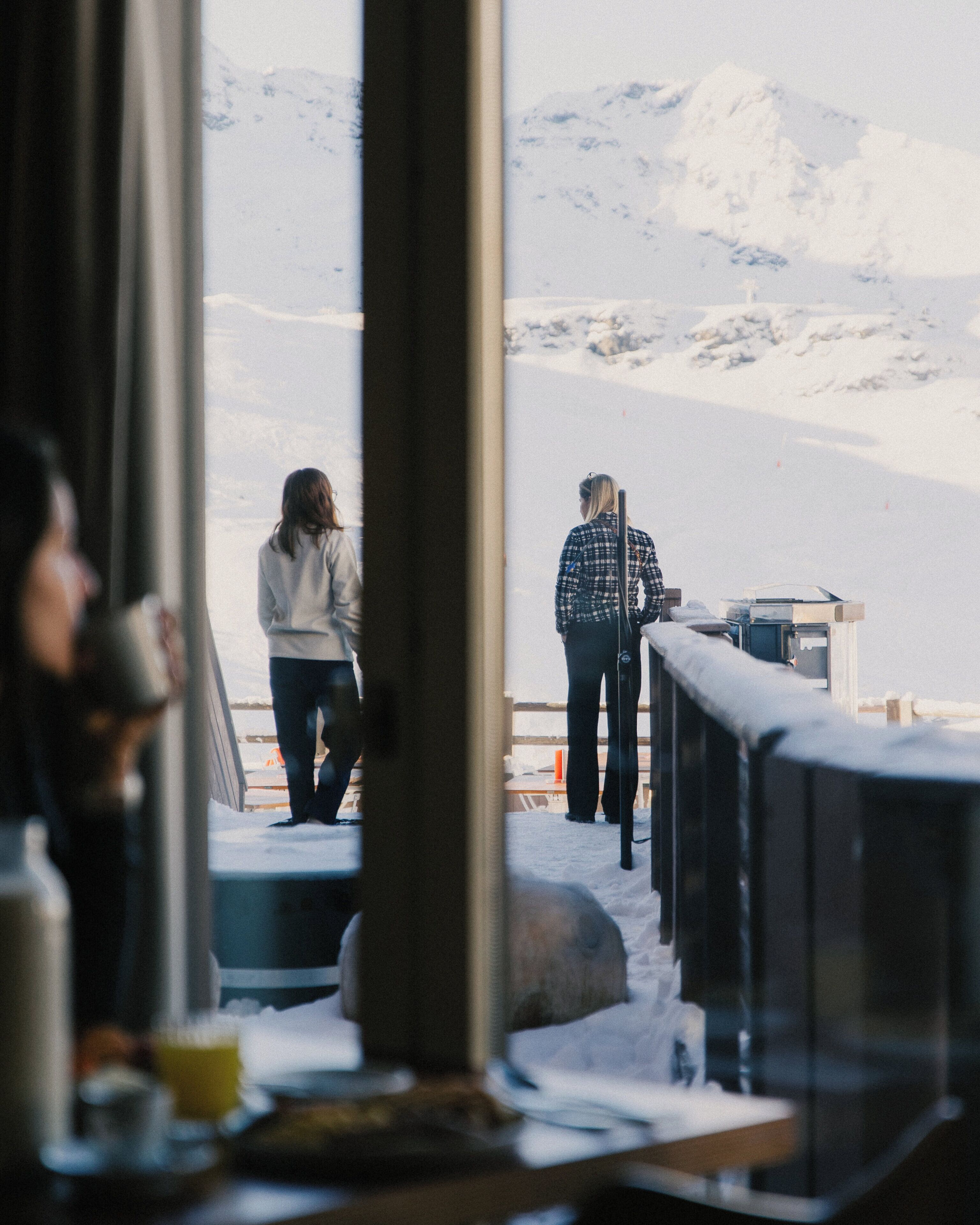 A view of a snowy landscape through a window, with a person standing on a deck.