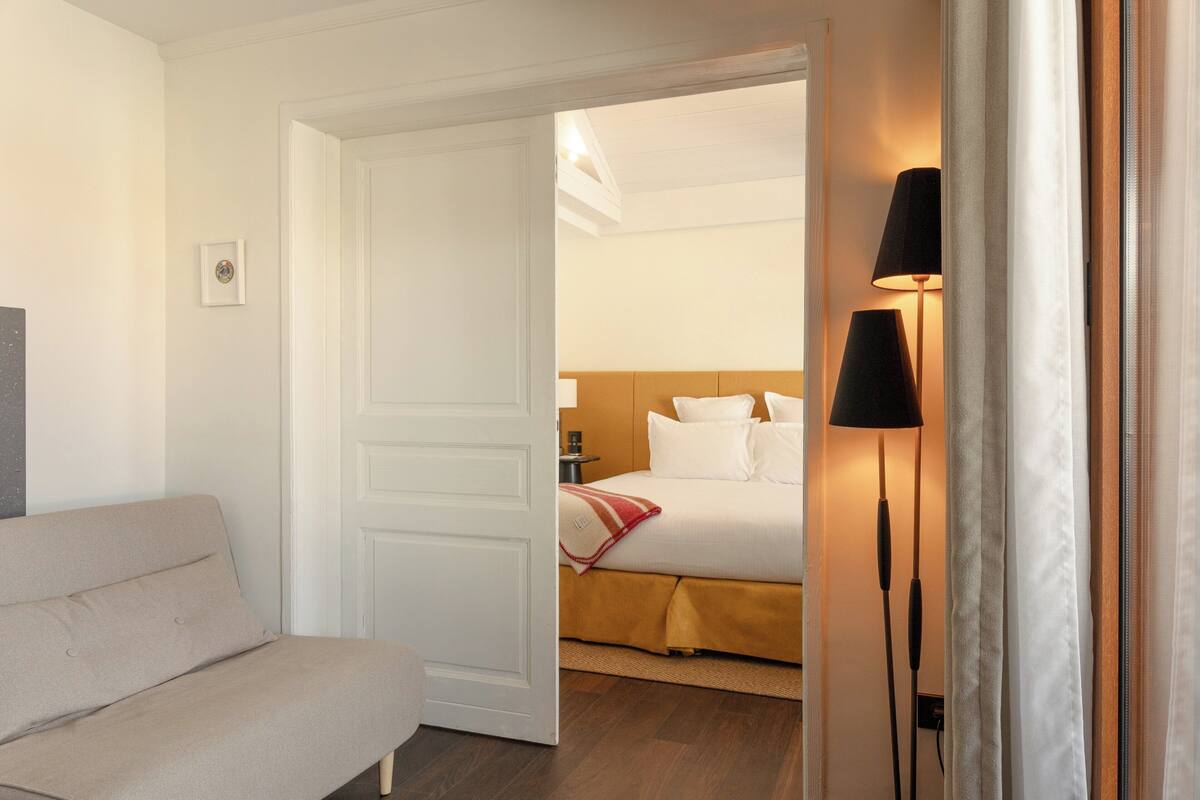 A hotel room with a bed, a bedside table, a lamp, and a sofa.