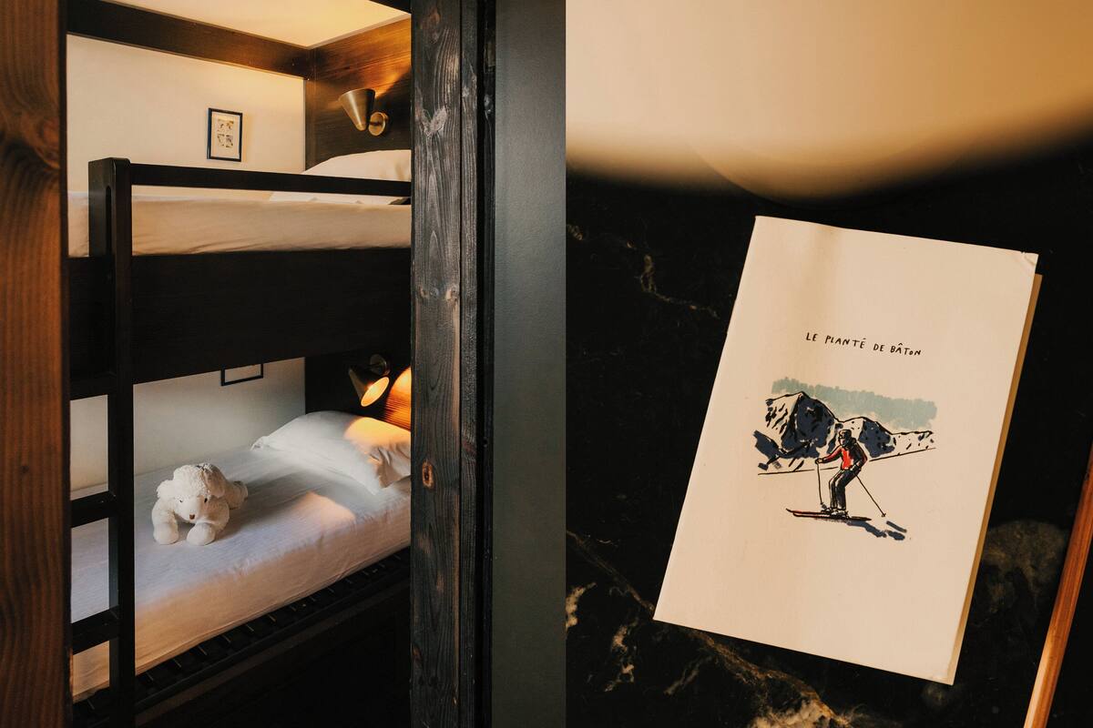 A bunk bed with a small bedside table, a lamp, and a teddy bear. There is a framed picture on the wall above the bed.