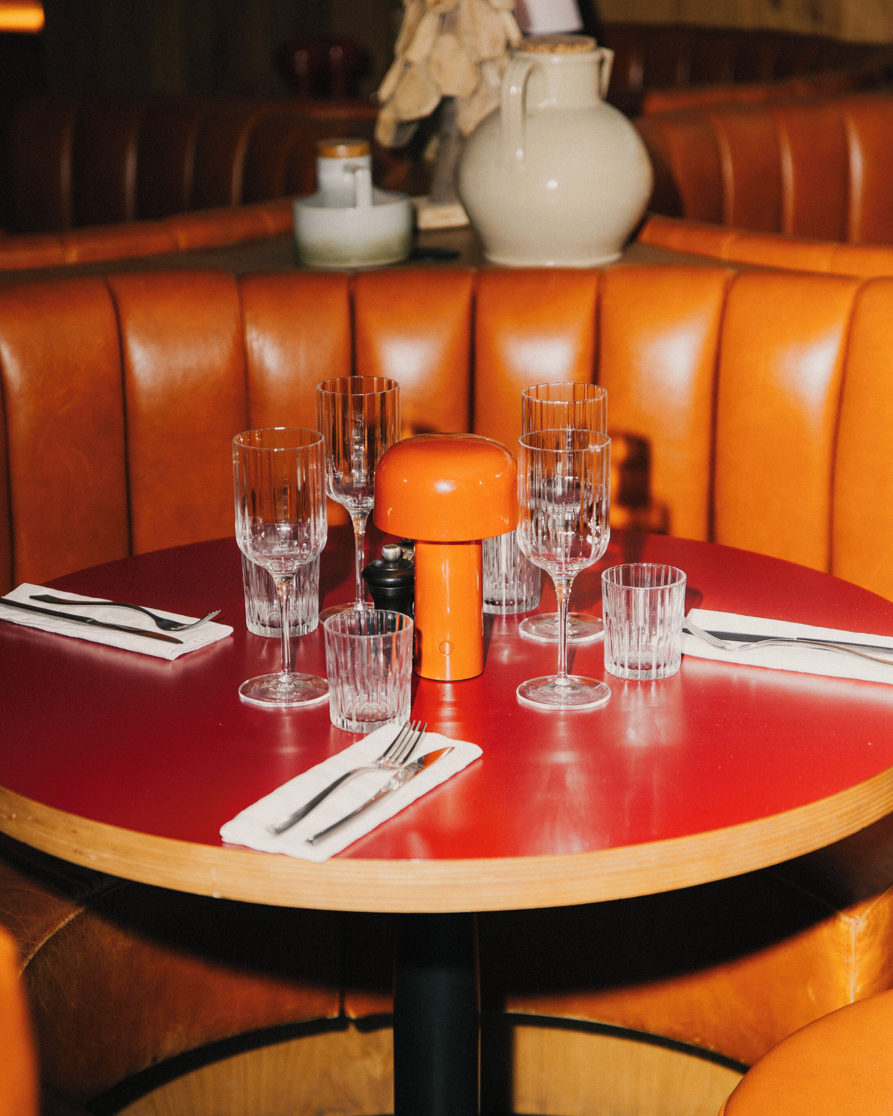 A dining table with a red surface, surrounded by orange leather booth seating.