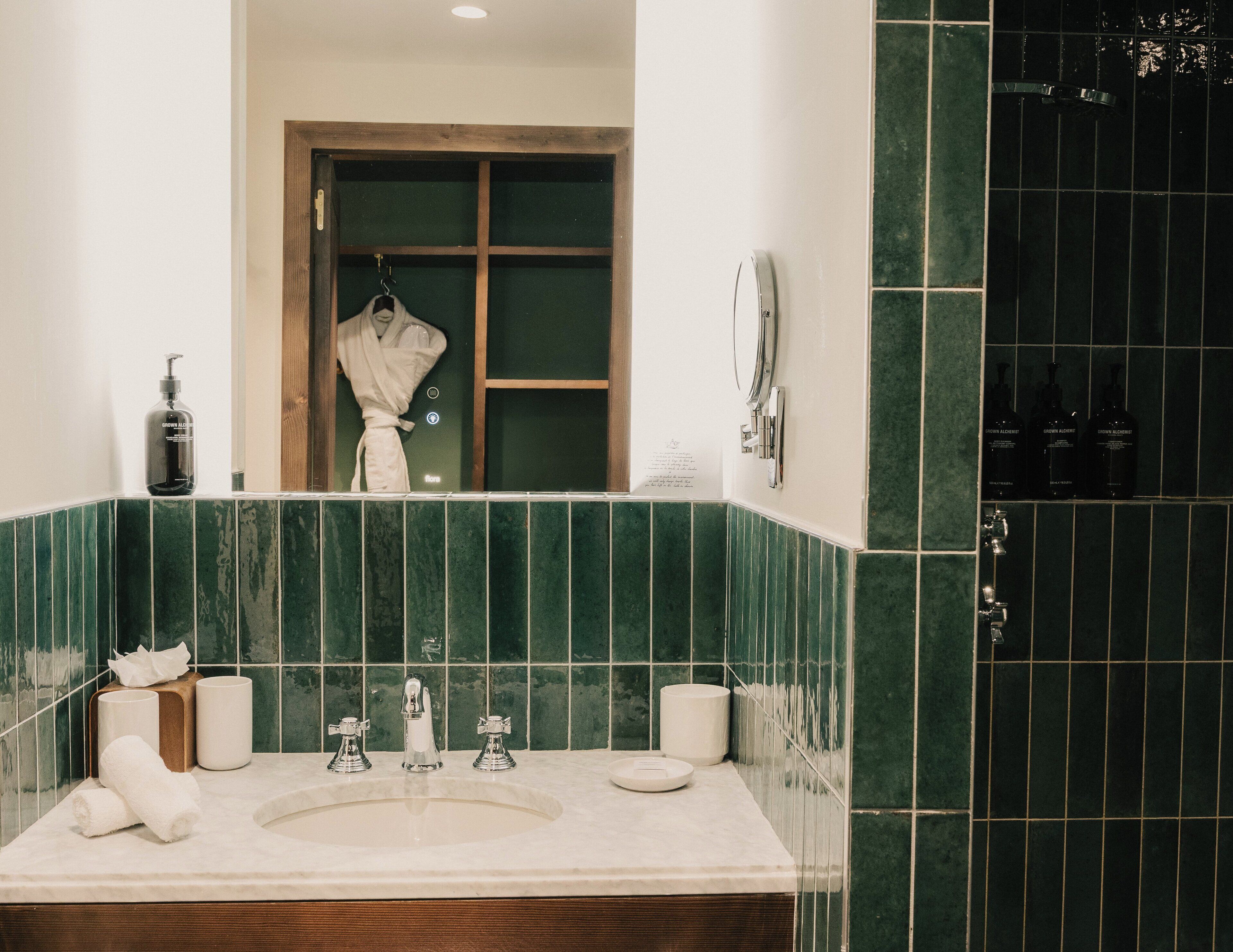 A bathroom with a large mirror, two sinks, a towel rack, and a robe hanging in the mirror.