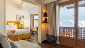 A hotel room with a bed, a sofa, a chair, a lamp, and a view of a snowy mountain. - Le Val Thorens, a Beaumier Hotel (Les Belleville)