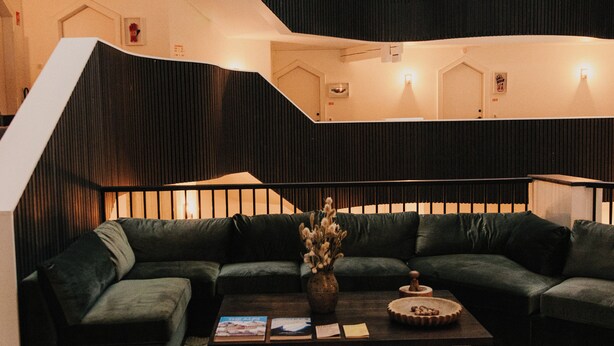 A modern interior with a green sofa set, a coffee table with books and a vase, and a brown ottoman. - Le Val Thorens, a Beaumier Hotel (Les Belleville)