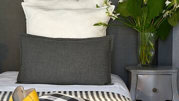 A neatly arranged bedroom with a bed, pillows, a bedside table, a vase with flowers, a yellow handbag, and a book.
