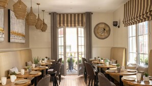A dining area with round tables, chairs, and a view through a doorway to an outdoor space. - Hotel Le Fer à Cheval (Trouville-sur-Mer)