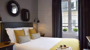 A hotel room with a bed, two wall mirrors, a bedside lamp, a window with curtains, and a view of the outside.