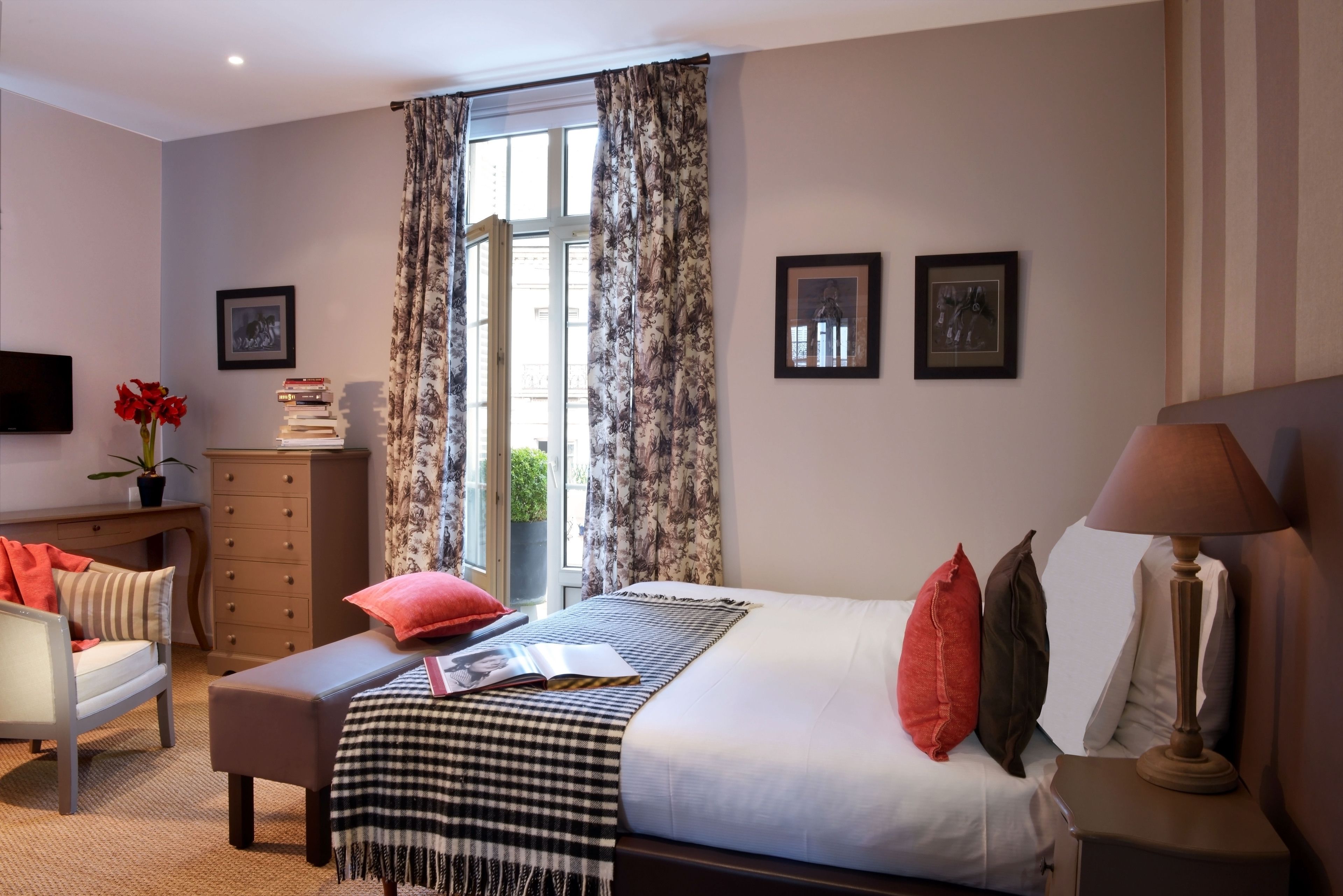 Habitación de hotel con cama, mesita de noche, lámpara, sillón, escritorio, cómoda y televisor.