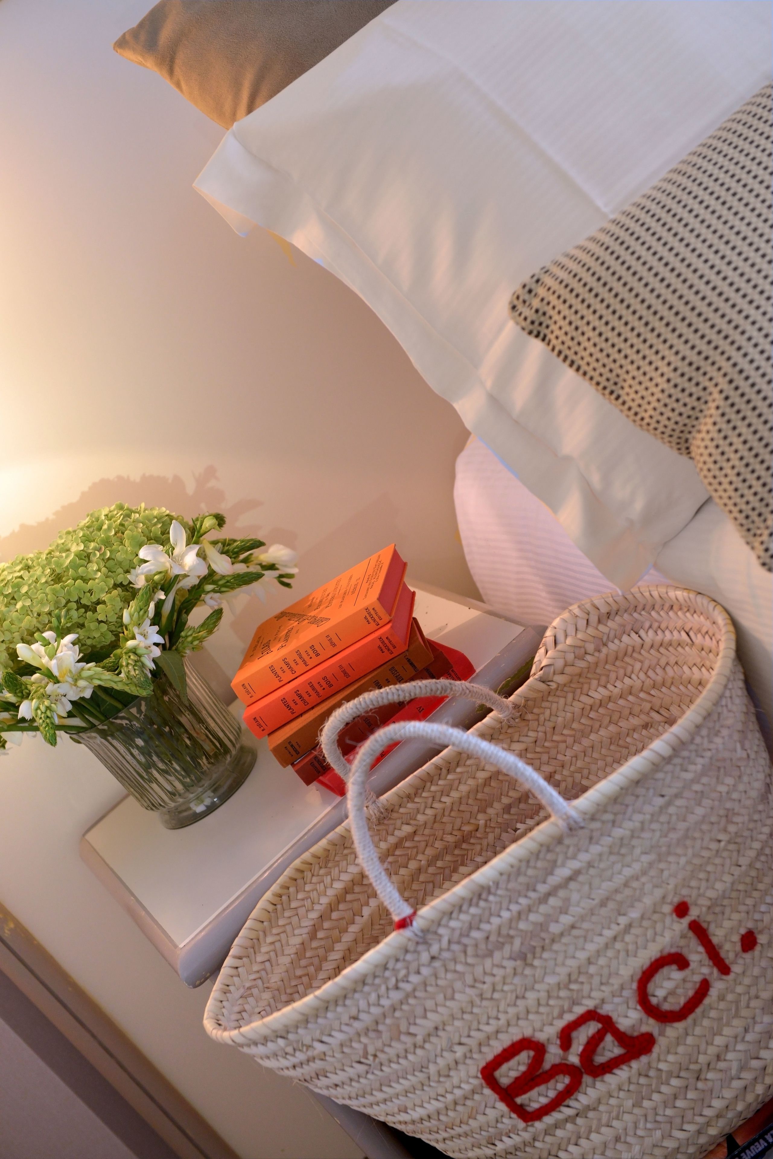 A neatly arranged room with a white sofa, a vase with flowers, a woven basket, and a stack of books.