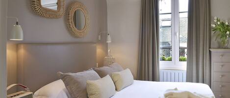 A bedroom with a large bed, two wall-mounted mirrors, a lamp, a dresser, and a window with curtains.