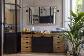 A kitchen with a wooden cabinet, a mirror, and a plant. - Hotel Le Fer à Cheval (Trouville-sur-Mer)